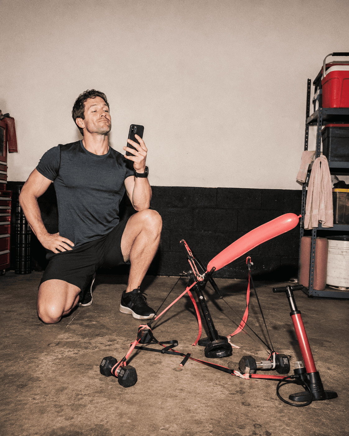A fully clothed man admiring an absurd homemade contraption built from gym equipment and a balloon